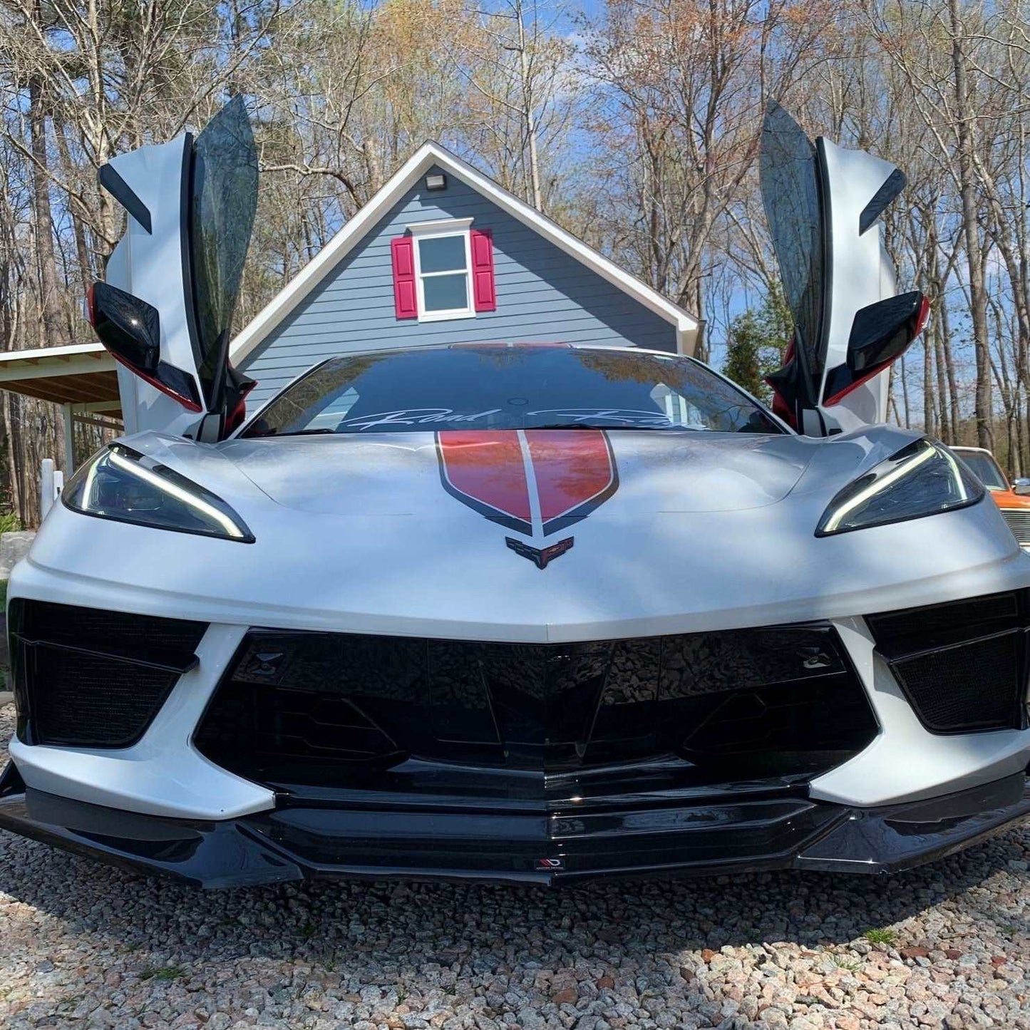 White sports car with C8 vertical doors at-home installation open in front of house with trees