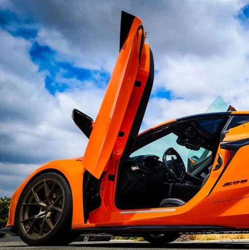 Orange sports car with C8 Z06 vertical door kit installed showing open scissor door and interior