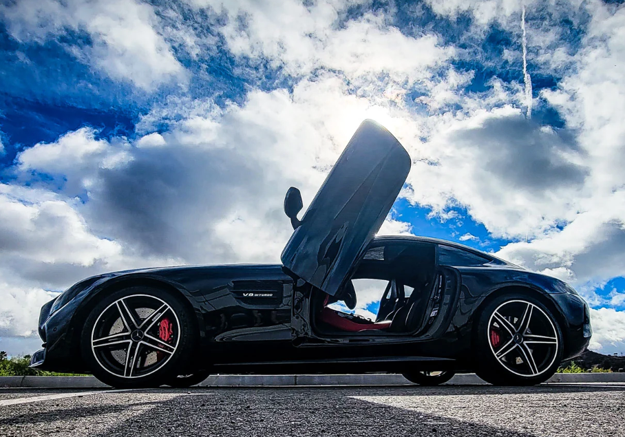 Black Mercedes AMG GT with one door open showcasing Mercedes AMG GT lambo doors kit under a cloudy sky