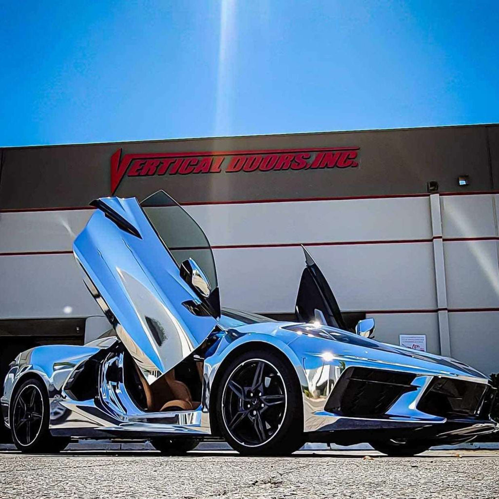 Chrome sports car with C8 vertical doors at-home installation by Vertical Doors Inc in front of building
