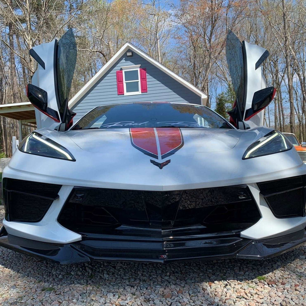 White sports car with C8 vertical doors at-home installation open in front of house with trees