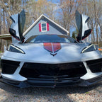 White sports car with C8 vertical doors at-home installation open in front of house with trees