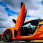 Orange sports car with C8 Z06 vertical door kit installed showing open scissor door and interior