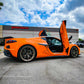Orange sports car with C8 Z06 vertical door kit installed and doors open in front of Vertical Doors Inc building