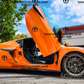 Orange sports car with C8 Z06 vertical door kit installed showing open scissor style doors