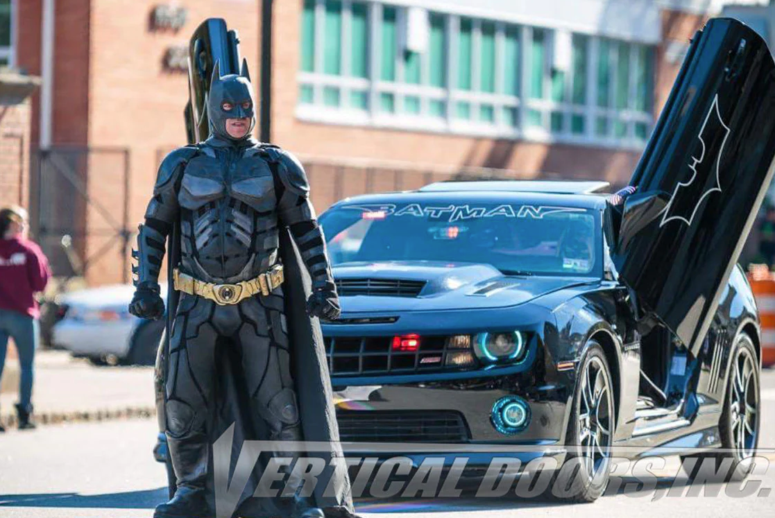 Black Camaro with bat logo on vertical doors open and Batman costume figure standing beside using Camaro vertical doors kit
