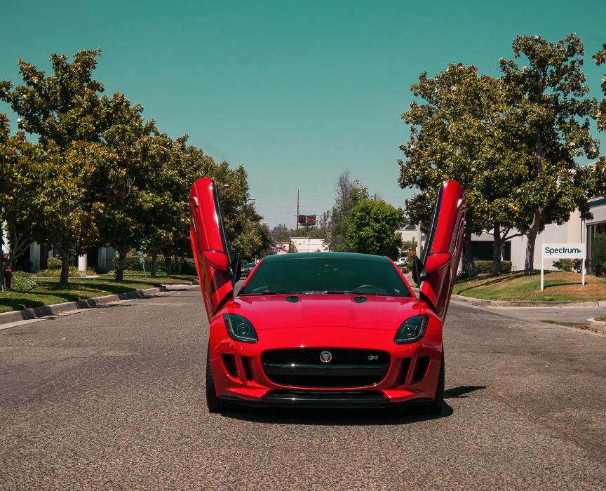Red Jaguar F-Type with installed Jaguar F-Type Lambo doors kit open on both sides on a sunny street