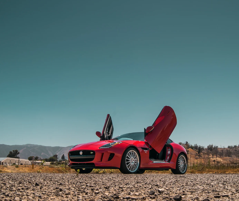 Red Jaguar F-Type sports car with Jaguar F-Type Lambo doors kit installed open on a sunny day