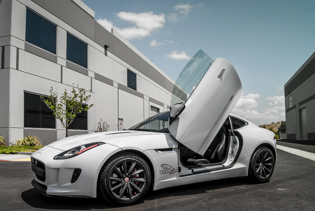 White Jaguar F-Type with Jaguar F-Type Lambo doors kit installed parked outside modern building