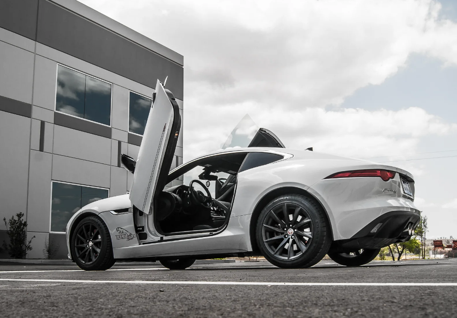 Silver Jaguar F-Type with Jaguar F-Type Lambo doors kit installed parked near modern building