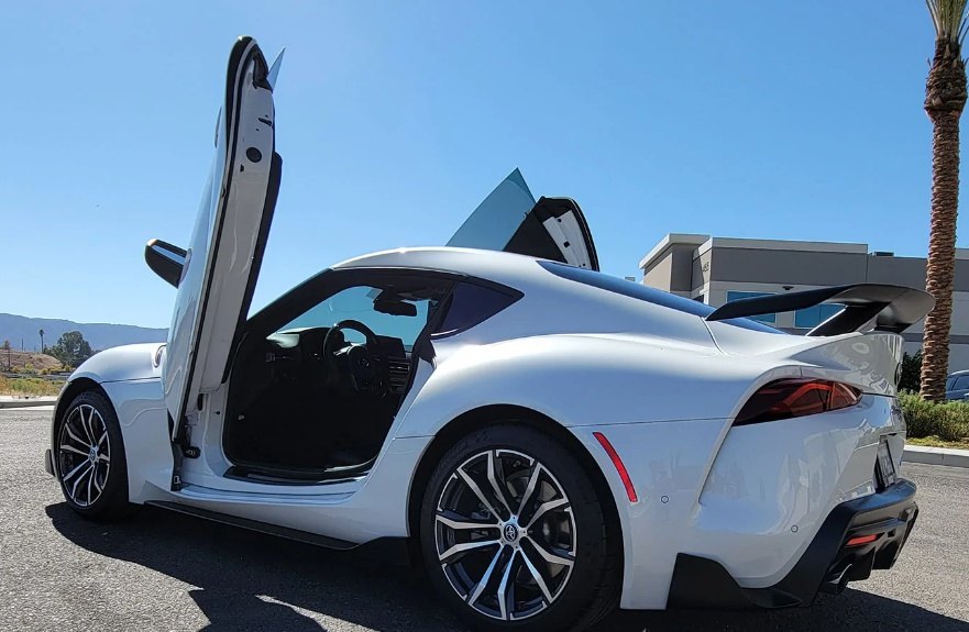 White Toyota Supra Mk5 with Toyota Supra Mk5 Lambo Doors open in a sunny outdoor setting